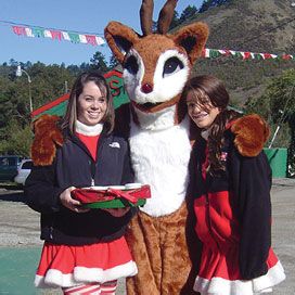 person in Rudolph costume with his arms around two of santa’s helpers