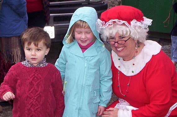 two small children standing with a smiling mrs. claus