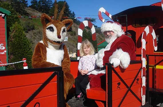 person in rudolph costume, small girl, and santa riding in an open red train car