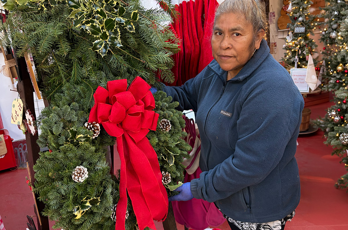 hispanic woman holding a beautiful green wreath with pine cones and red ribbon